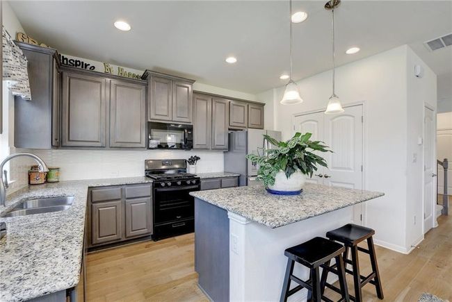 Kitchen featuring black appliances, a sink, light wood-style flooring, a kitchen island, and a breakfast bar area | Image 12