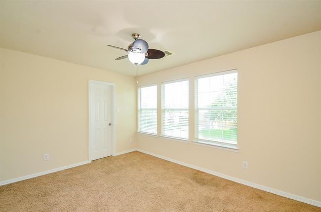 This secondary bedroom features neutral walls, carpeted flooring, a ceiling fan with light, and a window with blinds offering natural light. It's a versatile space suitable for a bedroom or office. | Image 27