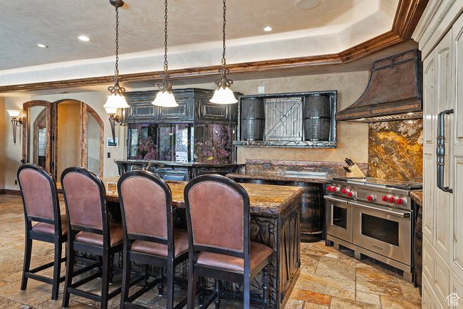 Kitchen featuring custom exhaust hood, arched walkways, a tray ceiling, double oven range, and stone tile floors | Image 49