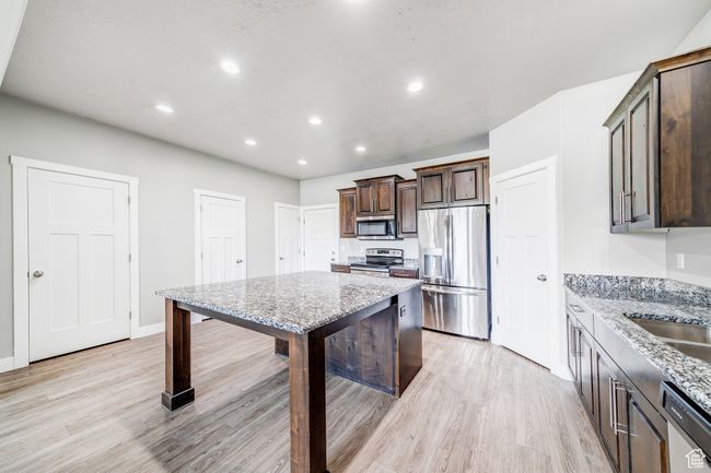 Kitchen with light wood-style flooring, light stone counters, stainless steel appliances, dark brown cabinets, and recessed lighting | Image 8