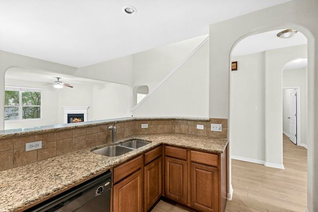 Kitchen featuring dishwashing machine, light stone counters, ceiling fan, backsplash, and brown cabinets | Image 11