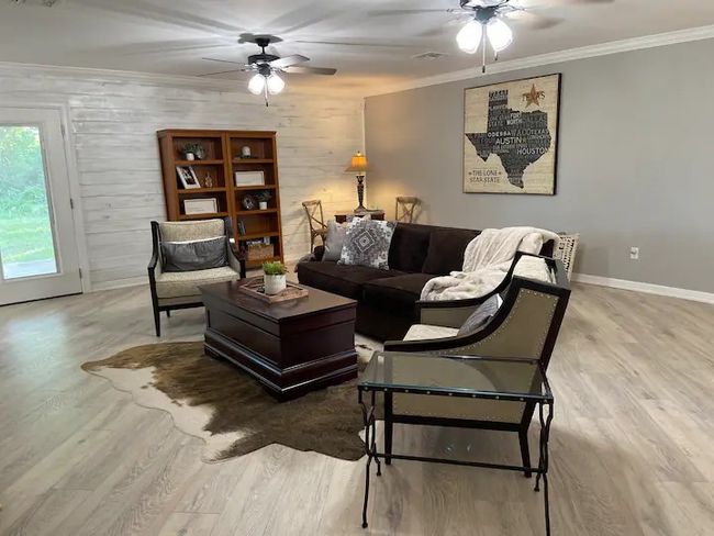 Living room with ceiling fan, wooden walls, light hardwood / wood-style flooring, and ornamental molding | Image 5