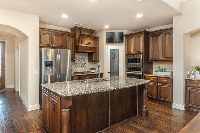Kitchen featuring appliances with stainless steel finishes, light stone counters, dark wood-style floors, arched walkways, and recessed lighting | Image 9