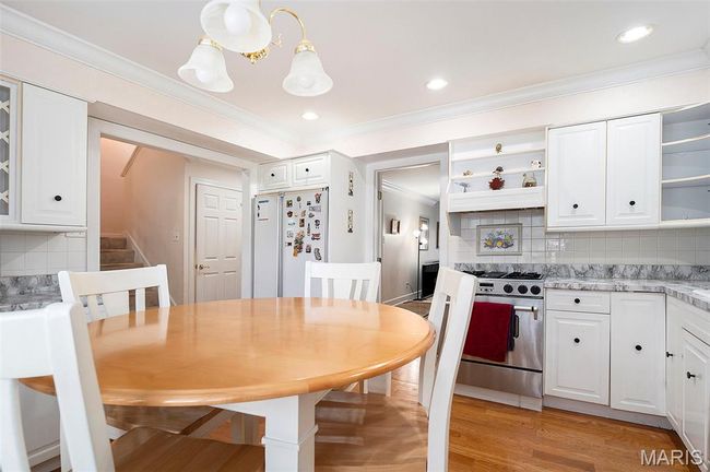 Kitchen featuring stainless steel gas stove, open shelves, freestanding refrigerator, ornamental molding, and white cabinetry | Image 7