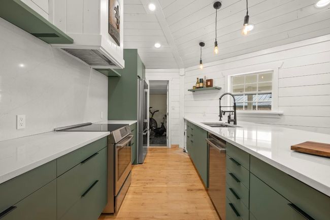 Kitchen with light wood-type flooring, pendant lighting, a sink, stainless steel appliances, and green cabinetry | Image 13