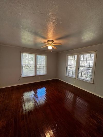 Spare room featuring a textured ceiling, ceiling fan, ornamental molding, and wood-type flooring | Image 3