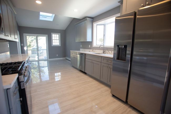 Kitchen featuring light stone countertops, sink, stainless steel appliances, lofted ceiling with skylight, and gray cabinets | Image 10