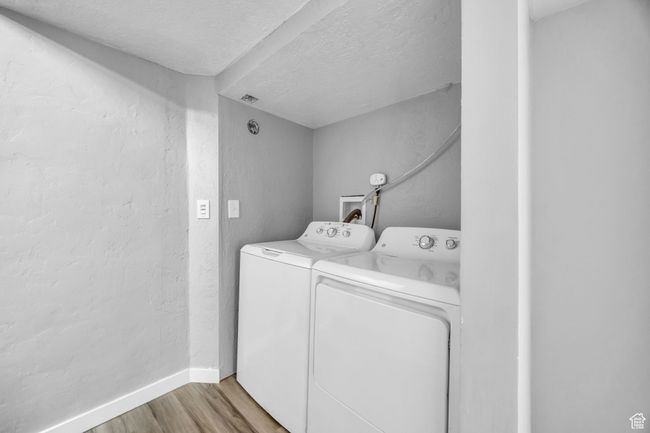 Laundry area featuring washer and dryer, light wood-type flooring, a textured ceiling, baseboards, and a textured wall | Image 26
