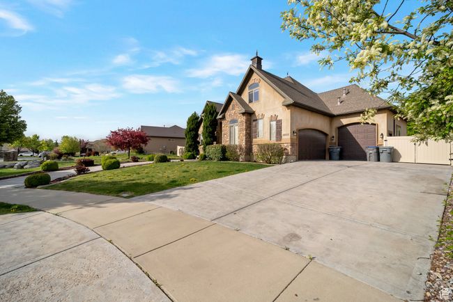French provincial home featuring a front yard, a garage, stone siding, concrete driveway, and stucco siding | Image 41