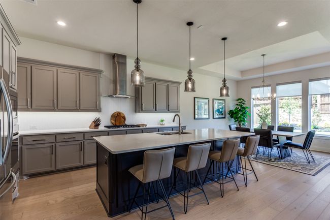 Kitchen featuring wall chimney range hood, gray cabinetry, tasteful backsplash, stainless steel gas cooktop, and a center island with sink | Image 14
