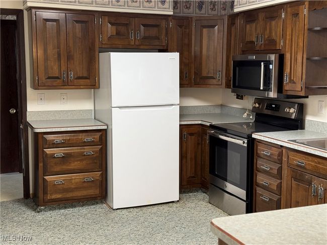 Kitchen with stainless steel appliances, light countertops, dark brown cabinetry, and open shelves | Image 16
