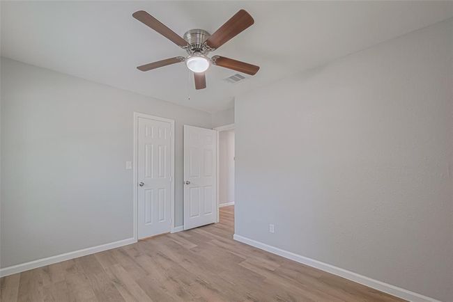 The third bedroom continues the theme of comfort with neutral tones, a ceiling fan, and wood-style flooring. | Image 22