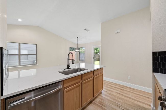 Kitchen featuring dishwasher, light wood-type flooring, lofted ceiling, hanging light fixtures, and light stone countertops | Image 14