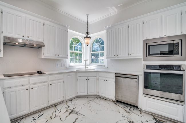 Kitchen with stainless steel appliances, under cabinet range hood, light countertops, light marble finish floors, and crown molding | Image 12