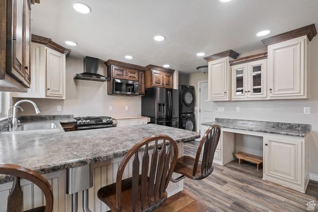 Kitchen with a sink, appliances with stainless steel finishes, stacked washer and clothes dryer, wall chimney exhaust hood, and a peninsula | Image 5