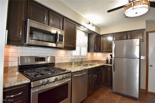 Kitchen featuring stainless steel appliances, a sink, dark brown cabinets, ceiling fan, and decorative backsplash | Image 11