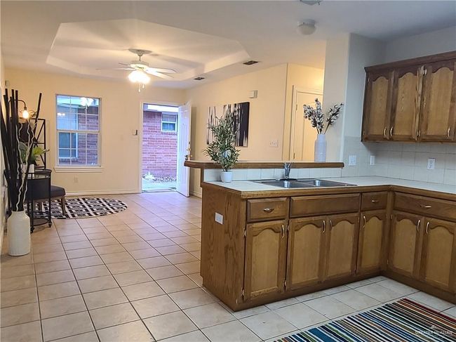 Kitchen with a sink, a tray ceiling, light tile patterned floors, a peninsula, and ceiling fan | Image 4