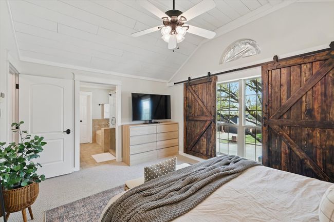 Carpeted bedroom with a barn door, lofted ceiling, wooden ceiling, ensuite bathroom, and ceiling fan | Image 17