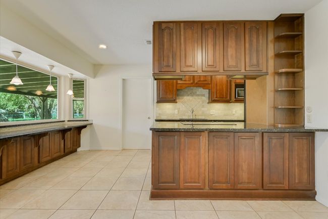 Kitchen featuring open shelves, backsplash, dark stone countertops, brown cabinets, and recessed lighting | Image 5