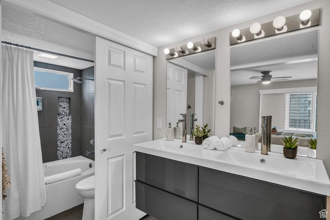 Full bath featuring double vanity, shower / bath combination with curtain, a textured ceiling, toilet, and a ceiling fan | Image 5