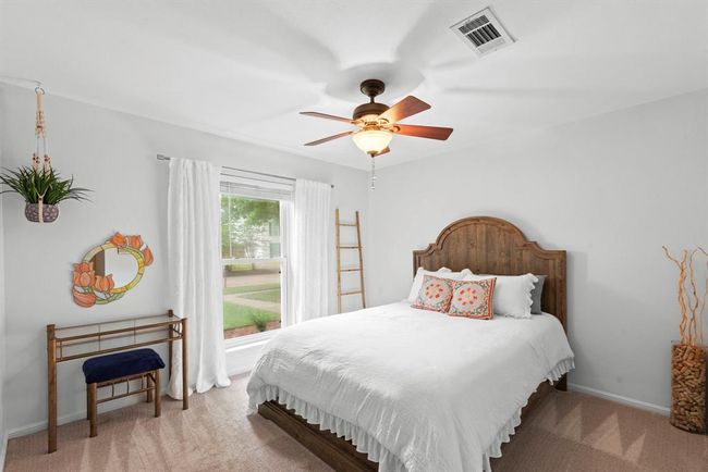 This bright bedroom features a ceiling fan and a large window offering a pleasant view and natural light. | Image 22