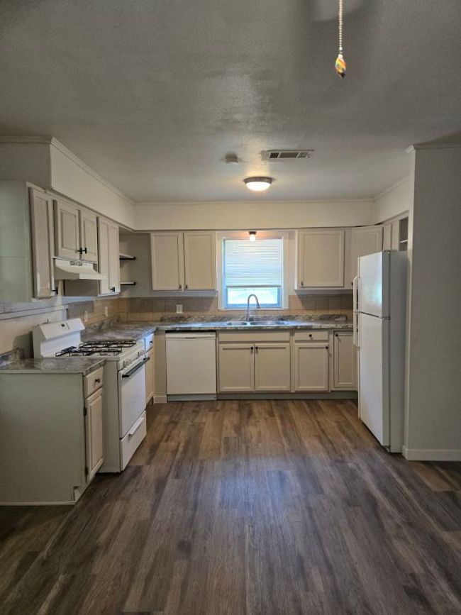 Kitchen with white appliances, under cabinet range hood, dark wood-type flooring, open shelves, and crown molding | Image 7