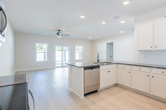 Kitchen with a sink, dark stone counters, stainless steel dishwasher, and a peninsula | Image 23