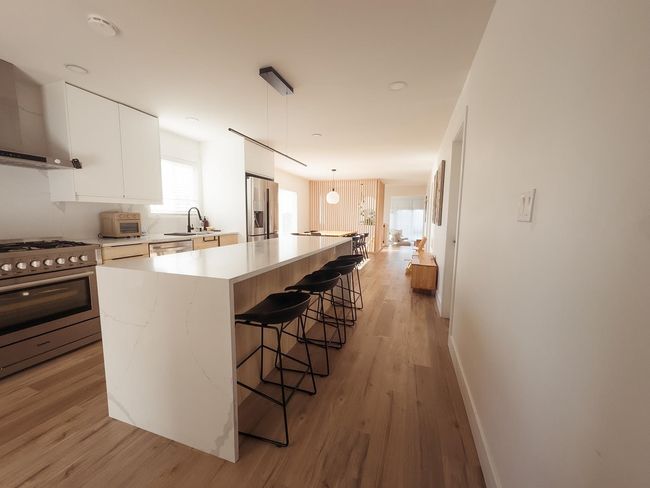 Kitchen featuring appliances with stainless steel finishes, wall chimney range hood, a sink, a kitchen bar, and light countertops | Image 7