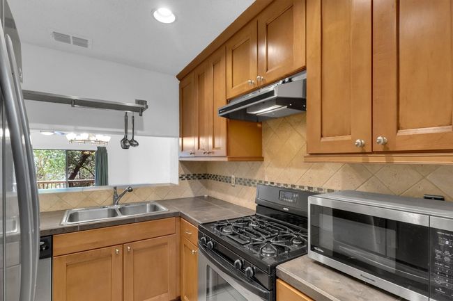 Kitchen with stainless steel microwave, backsplash, a sink, under cabinet range hood, and gas stove | Image 8