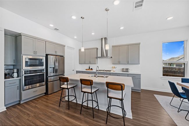 Kitchen featuring wall chimney range hood, gray cabinets, a breakfast bar, and stainless steel appliances | Image 4