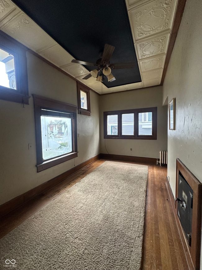 unfurnished living room featuring wood finished floors, baseboards, a tray ceiling, radiator heating unit, and a glass covered fireplace | Image 7