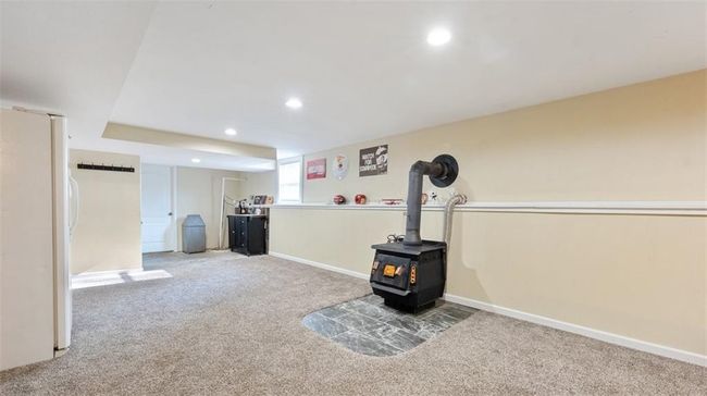 Below grade area featuring freestanding refrigerator, light carpet, recessed lighting, and a wood stove | Image 23