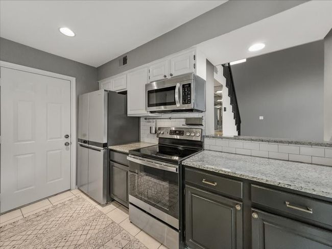 Kitchen with white cabinetry, tasteful backsplash, light tile patterned floors, stainless steel appliances, and light stone countertops | Image 14