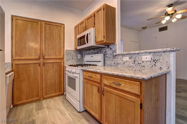Kitchen with white appliances, light wood finished floors, a ceiling fan, decorative backsplash, and light stone counters | Image 9