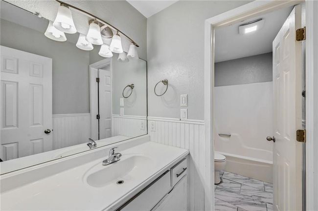 Full bathroom featuring marble look tiles, vanity, a wainscoted wall, toilet, and tub / shower combination | Image 14
