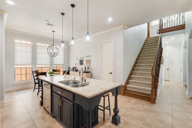 Kitchen with a breakfast bar area, stainless steel dishwasher, ornamental molding, light tile patterned floors, and light stone counters | Image 6