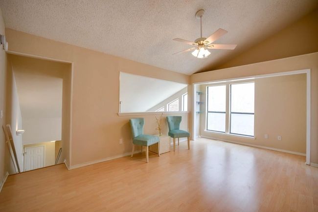 Living area featuring ceiling fan, vaulted ceiling, wood finished floors, a textured ceiling, and an upstairs landing | Image 8