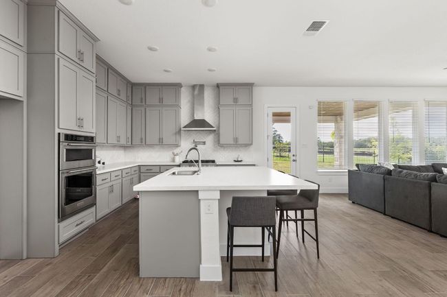 Kitchen featuring gray cabinetry, wall chimney range hood, stainless steel double oven, a sink, and light countertops | Image 12