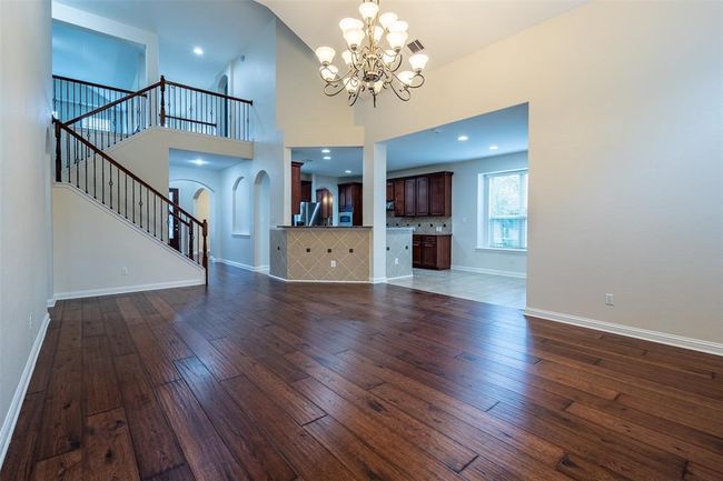 Unfurnished living room featuring dark wood-style flooring, a chandelier, stairs, arched walkways, and a towering ceiling | Image 4