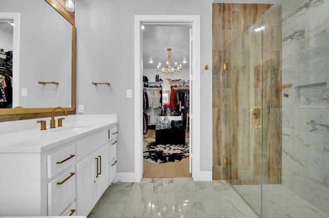Full bath featuring vanity, a walk in closet, marble look tiles, a stall shower, and a chandelier | Image 23
