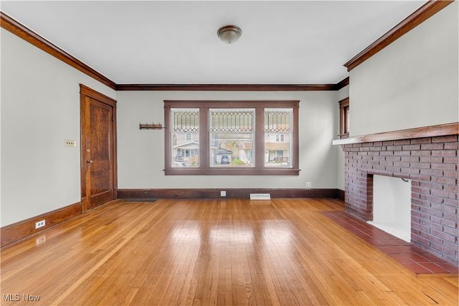 Unfurnished living room with visible vents, ornamental molding, light wood-style floors, and a fireplace | Image 5