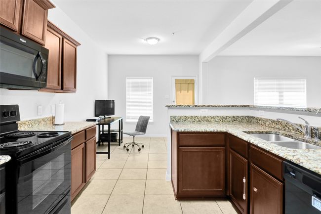 Kitchen featuring a sink, light tile patterned floors, black appliances, and light stone countertops | Image 14