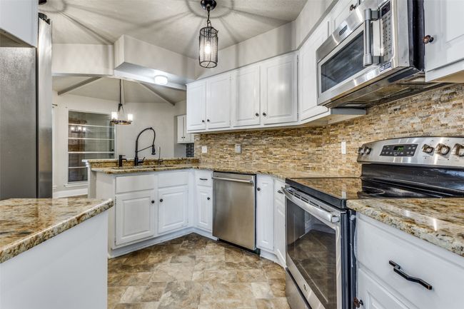 Kitchen featuring stainless steel appliances, white cabinetry, light stone counters, and hanging light fixtures | Image 8