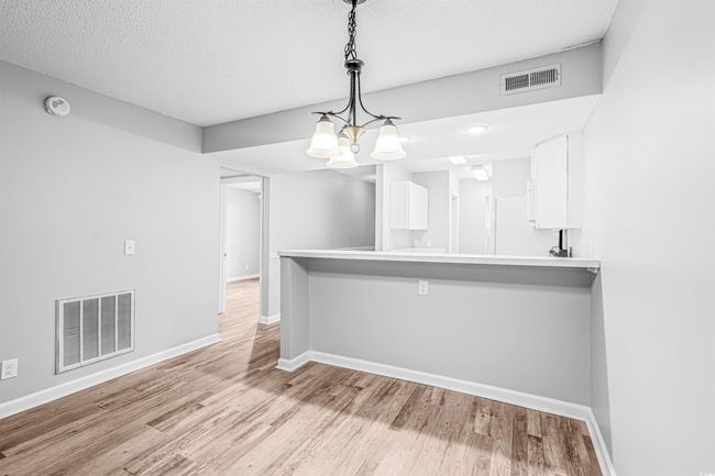 Kitchen with white cabinets, light wood-type flooring, a kitchen bar, hanging light fixtures, and a textured ceiling | Image 16