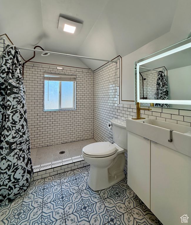 Bathroom with toilet, tile patterned floors, a tile shower, tile walls, and vaulted ceiling | Image 29