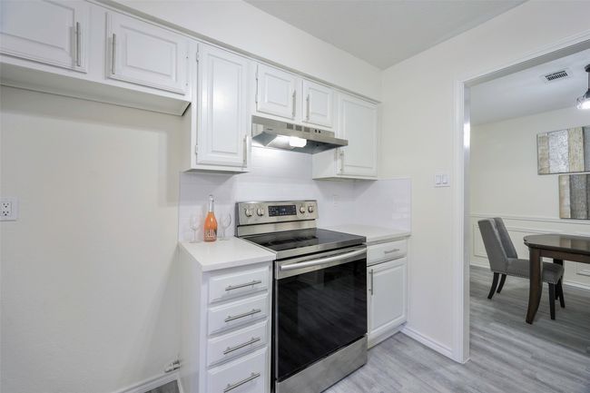Kitchen featuring visible vents, under cabinet range hood, light countertops, decorative backsplash, and electric range | Image 13