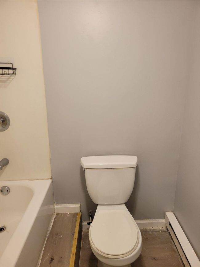 Bathroom featuring a baseboard radiator, baseboards, a tub to relax in, toilet, and a shower | Image 4