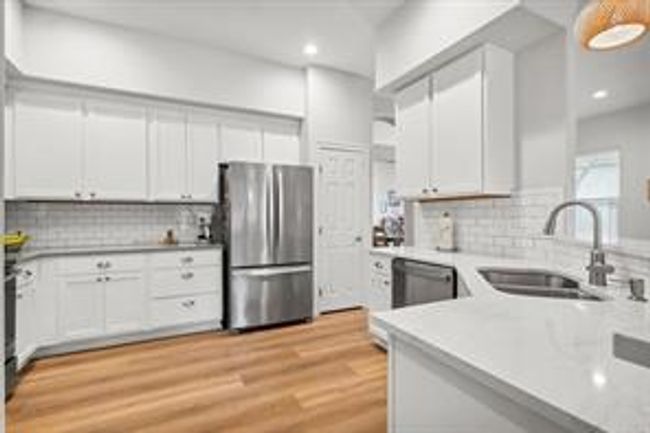 Kitchen with a sink, freestanding refrigerator, light wood-style floors, light countertops, and dishwashing machine | Image 12