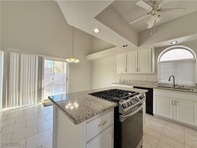 Kitchen with a sink, range with gas cooktop, light stone counters, and ceiling fan with notable chandelier | Image 14