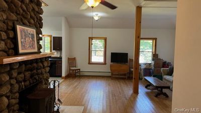 Living room with a baseboard heating unit, ceiling fan, light hardwood / wood-style floors, and a stone fireplace | Image 2